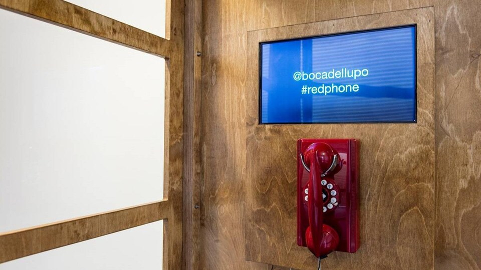 L'intérieur d'une cabine téléphonique, avec un téléphone rouge et un écran.