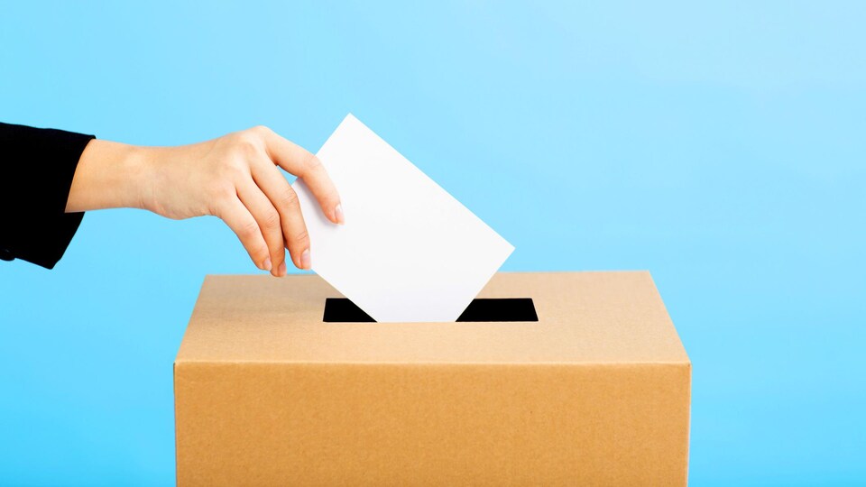 Une main dépose un bulletin de vote dans une boîte.