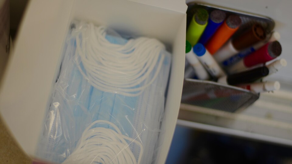 Masques chirurgicaux dans une boîte à côté d'un porte-crayons rempli.
