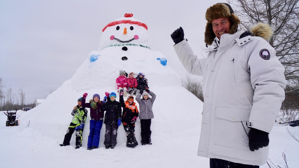 Un grand-père pose devant un bonhomme de neige.