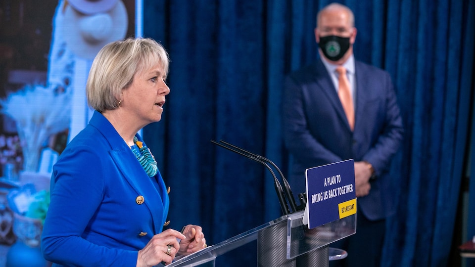 La médecin Bonnie Henry est au microphone avec le premier ministre de la Colombie-Britannique en arrière plan.