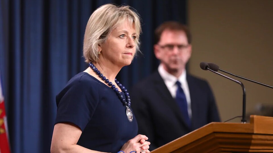 Plan épaules de Bonnie Henry devant des micros lors d'une conférence de presse.