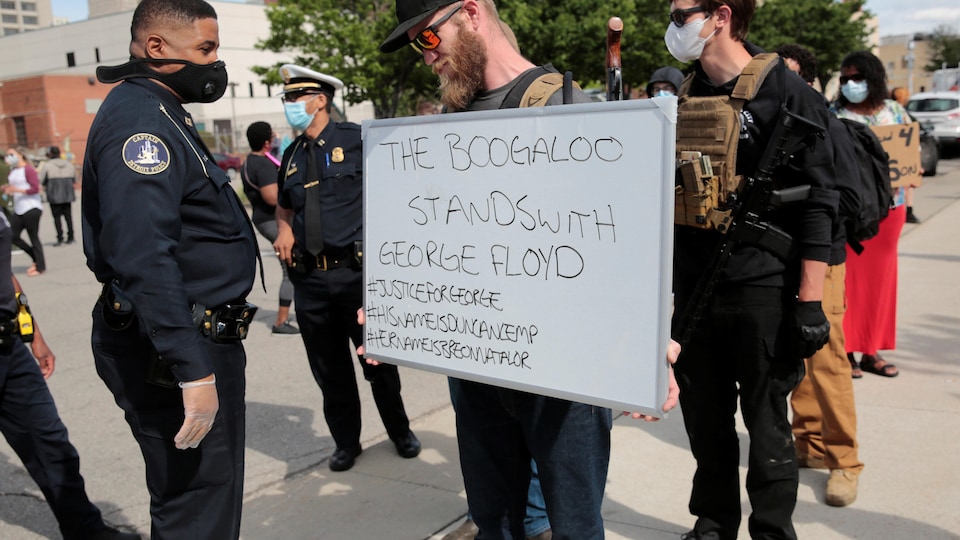 Un homme barbu tient un écriteau qui contient plusieurs mots-clics. "Les Boogaloo appuient George Floyd", est-il écrit.