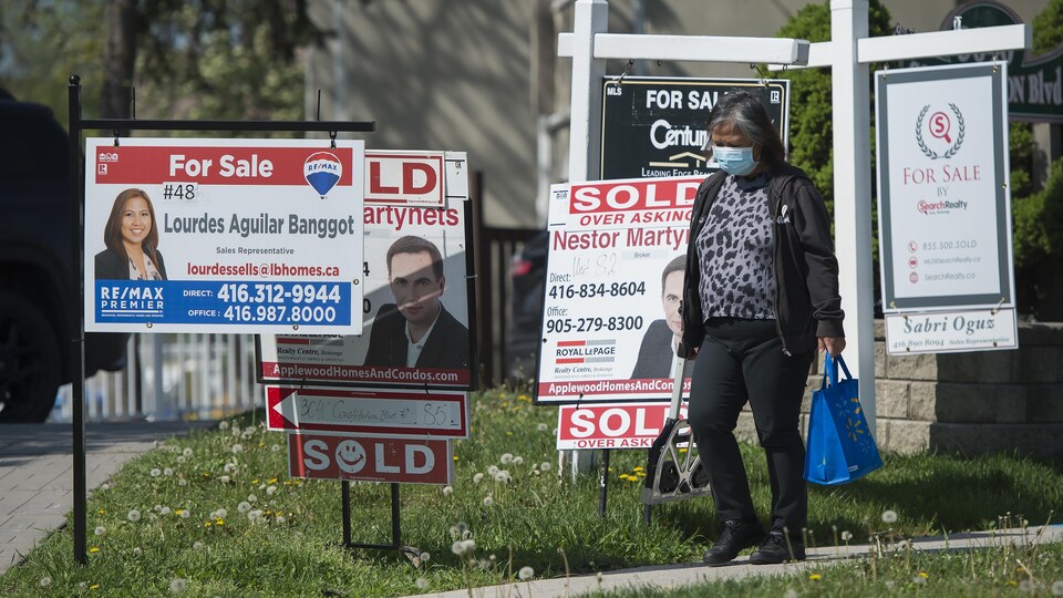 Une passante devant plusieurs panneaux de ventes immobilières.