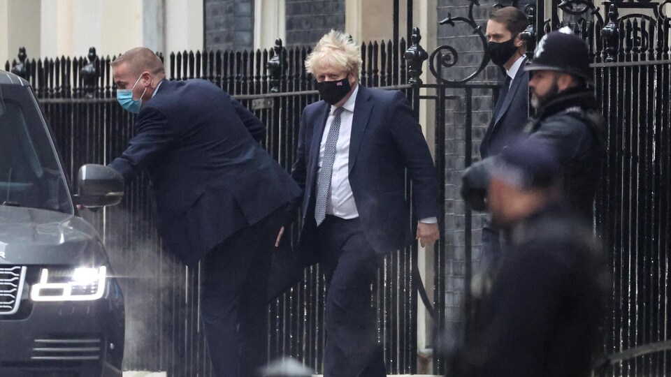 Boris Johnson, masqué, s'apprête à entrer dans une voiture.