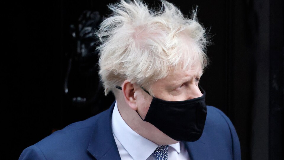 Boris Johnson, cheveux au vent, porte un masque.