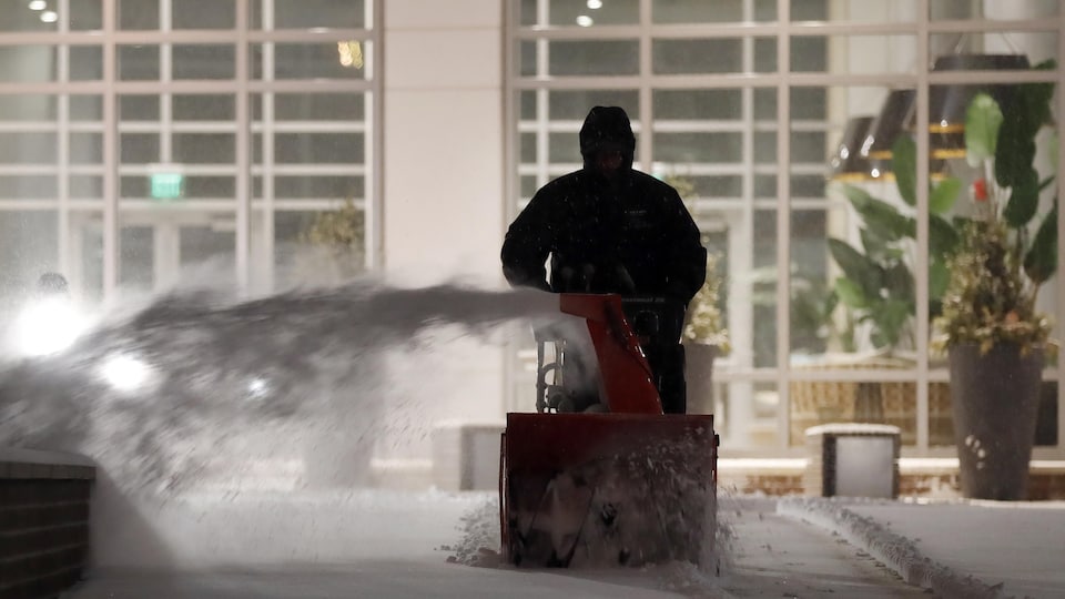 Un ouvrier déblaie le trottoir à l'aide d'une souffleuse à neige.
