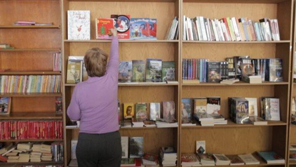 Une femme place un livre sur une étagère.