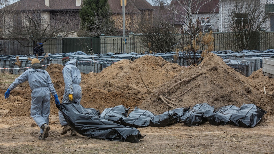 Deux personnes transportent un sac de plastique contenant une dépouille.