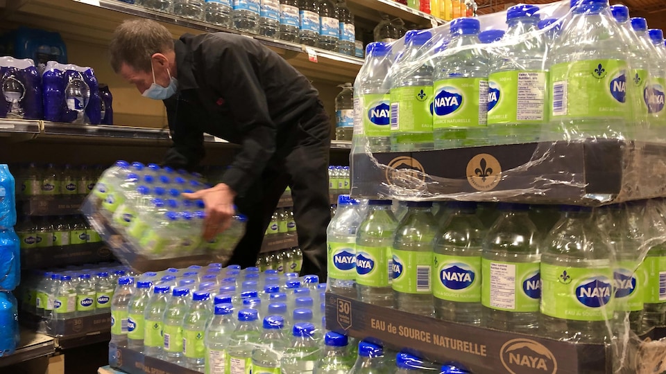Un commis d'épicerie du IGA Baril de Shawinigan remplit les étagères de bouteilles d'eau.