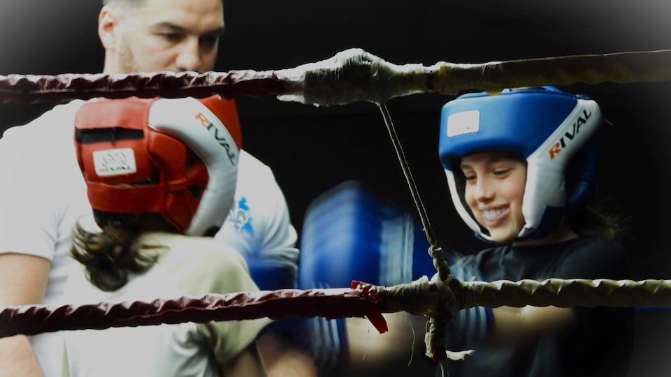 Deux jeune boxeurs, munis de casques de protection, se font face dans un ring sous le regard d'un arbitre.