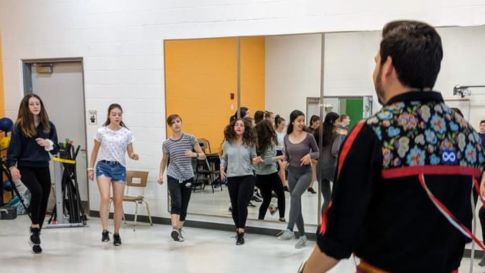 Un homme enseigne la danse à des jeunes dans un gymnase.