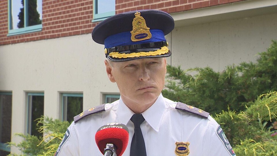 Un policier en uniforme coiffé d'un képi, debout à l'extérieur devant un microphone.
