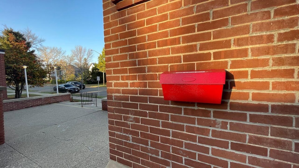 Une boîte aux lettrres rouge sur un mur de brique.