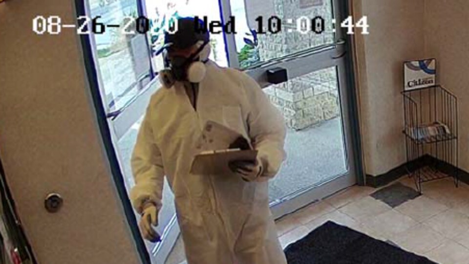 Un homme en combinaison blanche avec un masque filtrant dans une banque.