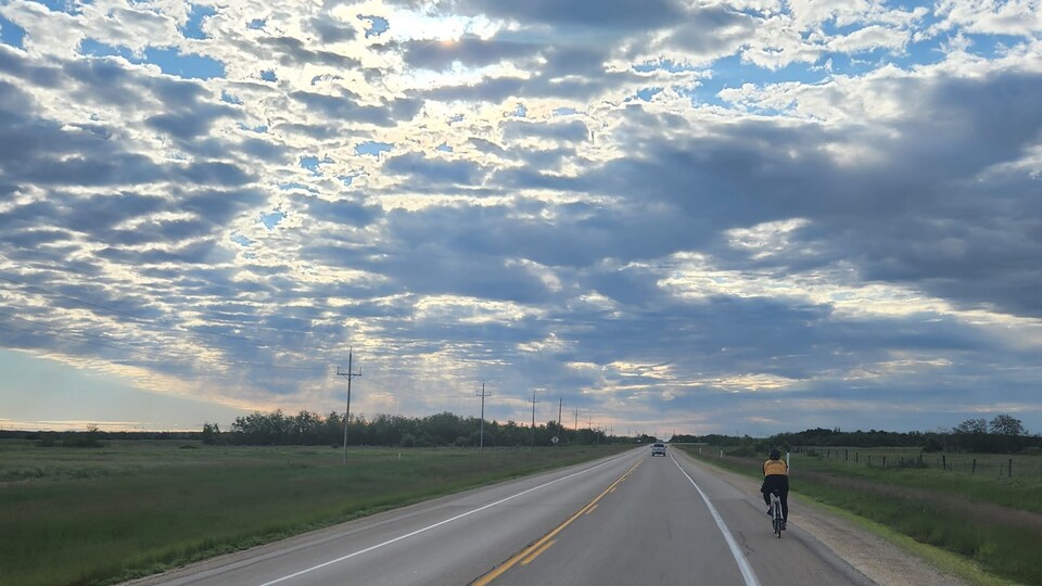 Une cycliste roule sur l'accotement d'une route au Manitoba, en fin de journée. 