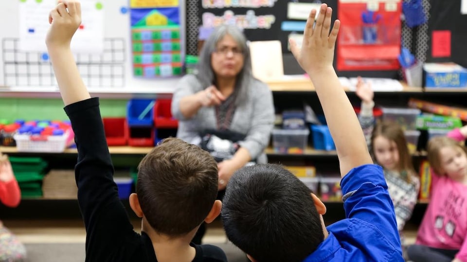 Deux élèves lèvent la main dans une salle de classe. 