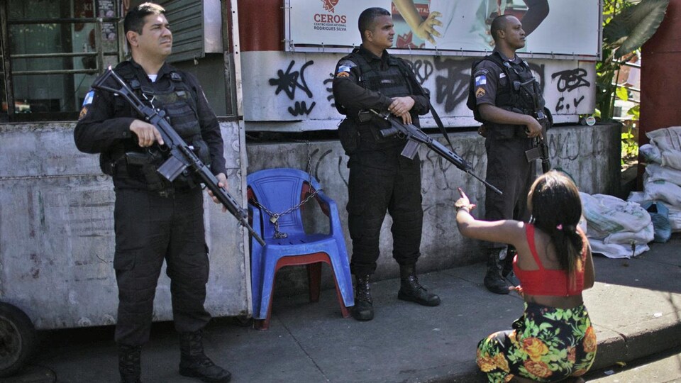 Une femme accroupie fait face à trois policiers dans une favela à Rio de Janeiro.