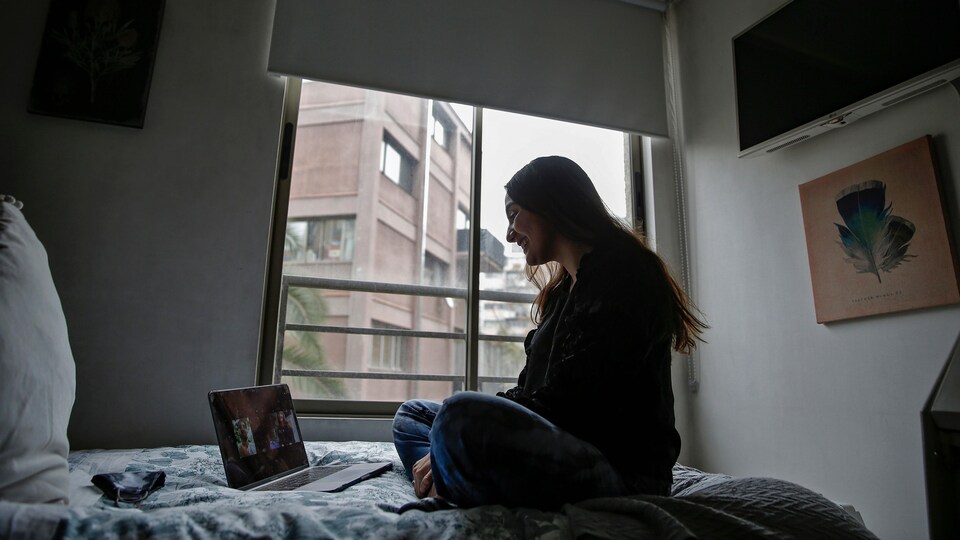Une jeune femme assise sur son lit parle avec son amoureux grâce à son ordinateur portable.