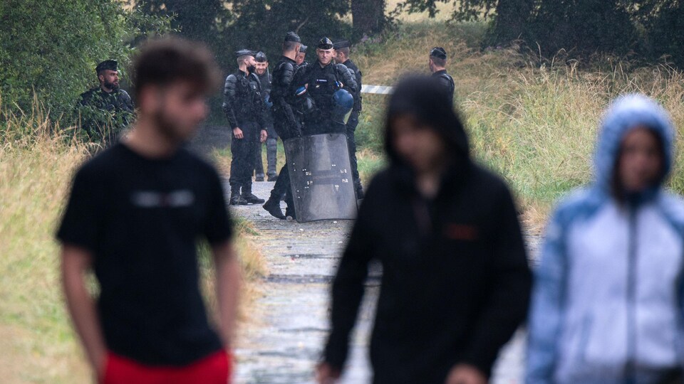 Des jeunes marchent sur un chemin de terre tandis que des policiers les regardent au loin.