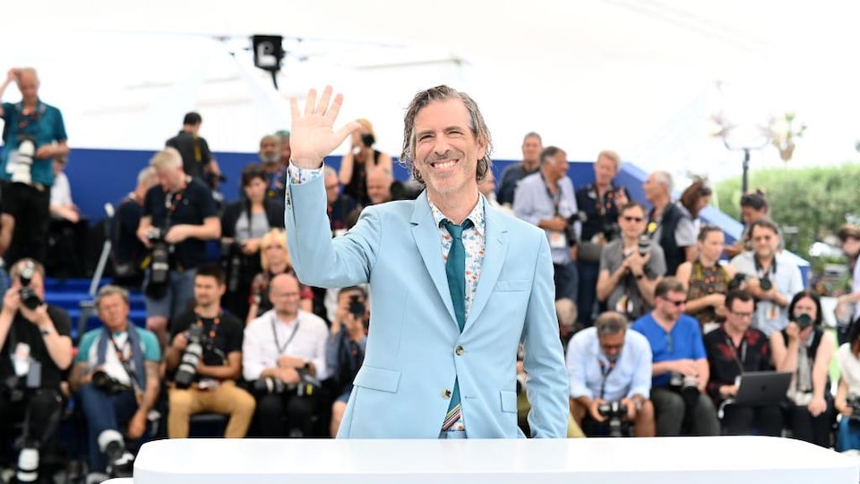 Smiling, the director held out his hand. Behind him, several photographers stood in bleachers.
