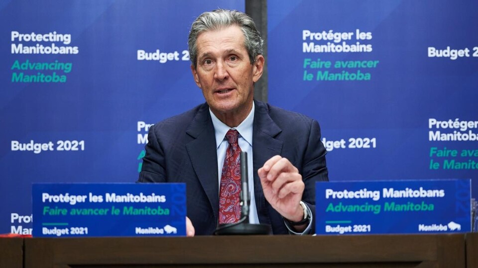 Brian Pallister assis à un bureau de conférence de presse.