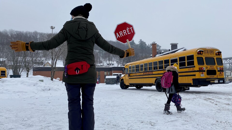 Une brigadière, une élève et un autobus scolaire devant l'école primaire Marguerite-D'Youville