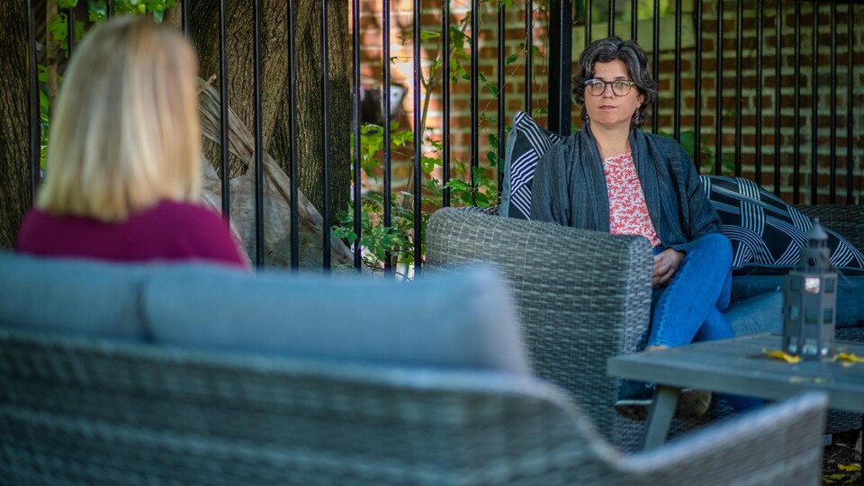 Claire Trottier regarde la journaliste Brigitte Bureau lors d'une entrevue dehors sur une terrasses en été. 