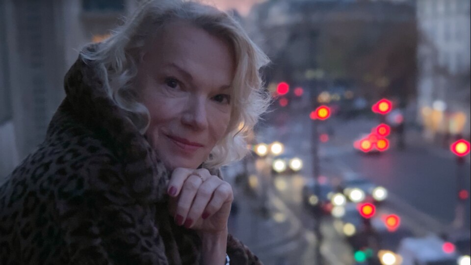 A woman posed on a balcony overlooking the street, her chin resting on her hand. 