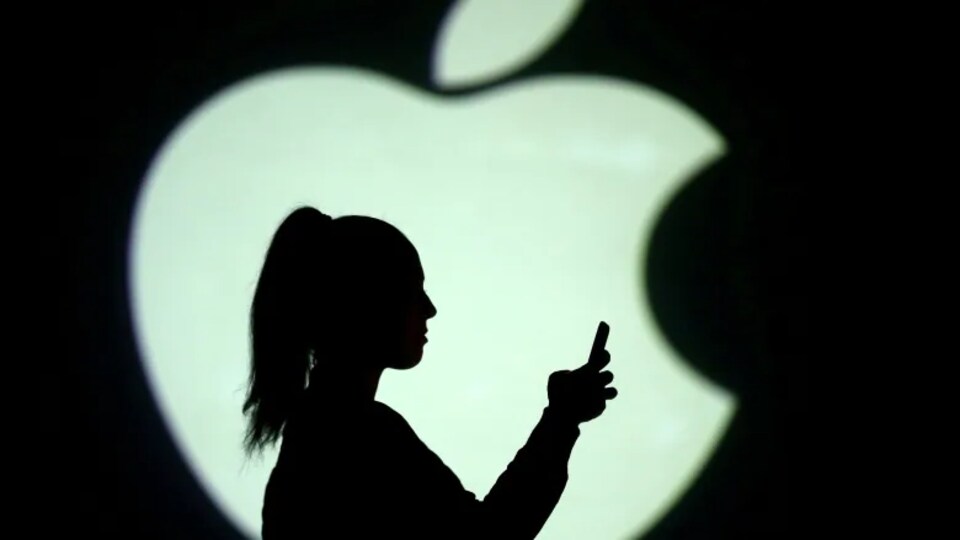 Silhouette d'une personne qui tient un téléphone intelligent devant un immense logo d'Apple.