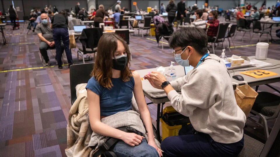 Une personne masquée se fait vacciner dans une grande salle.