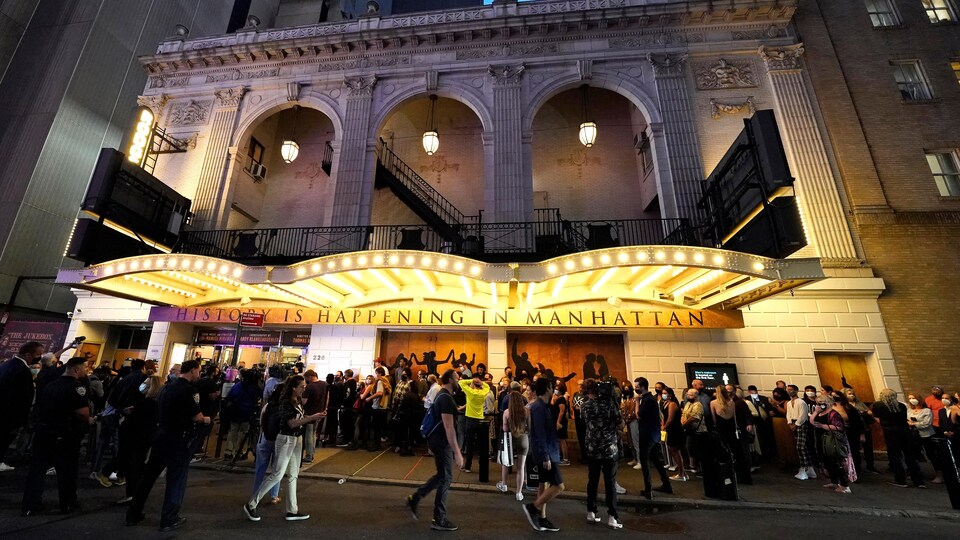 À l'extérieur, devant un théâtre, des personnes masquées attendent en ligne.