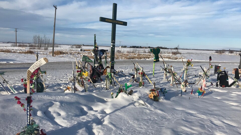 Des croix et des bâtons de hockey installés dans la neige, avec des fleurs, des drapeaux et des messages. 