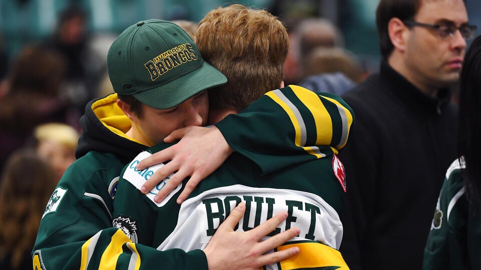 Deux jeunes hommes portant des chandails des Broncos s'enlacent.