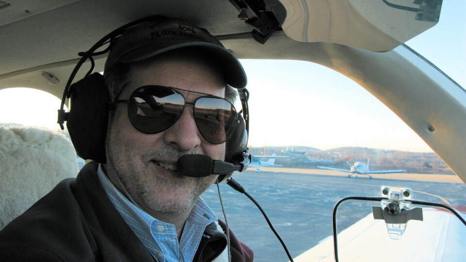 Un homme sourit à la caméra dans un petit avion, casque d'écoute sur la tête.