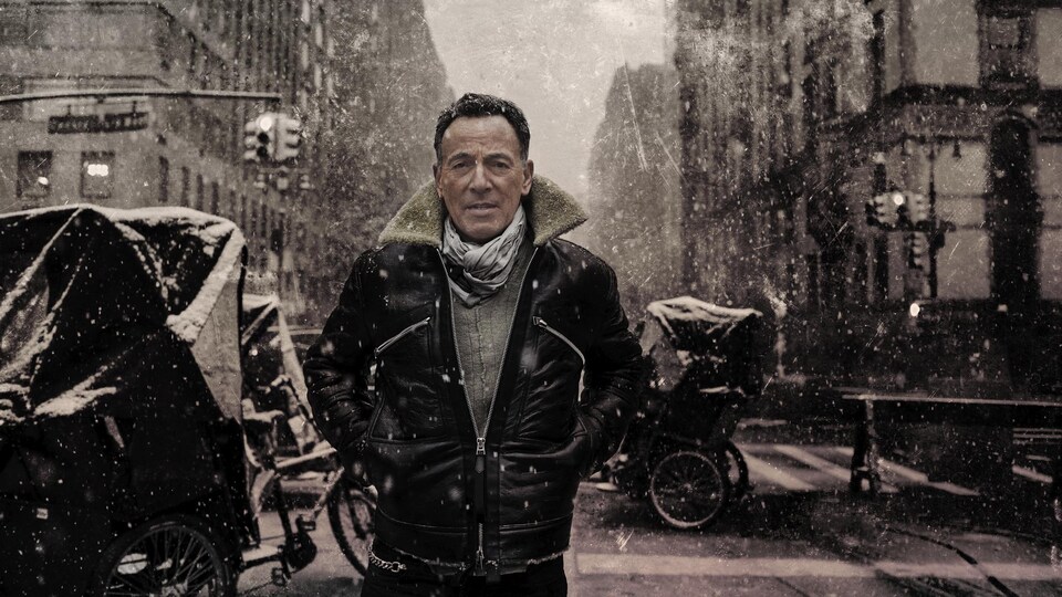 Bruce Springsteen, avec un manteau de cuir, pose dans une rue.