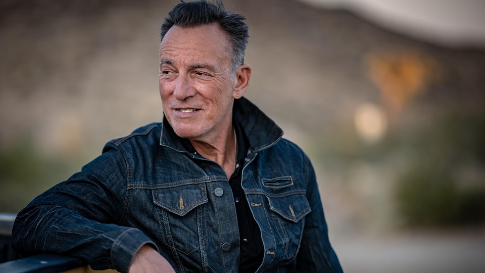 Bruce Springsteen sourit en regardant au loin. Il porte une veste en jeans.
