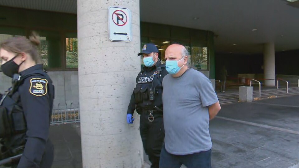 Vêtu d'un t-shirt, l'homme au crâne dégarni est escorté par deus policiers à l'extérieur du palais de justice