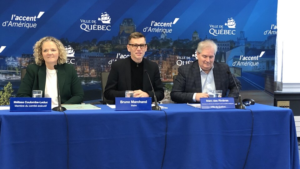Bruno Marchand lors d'un point de presse à l'hôtel de ville de Québec. Il est assis à une table avec, à ses côtés, Mélissa Coulombe-Leduc et Marc des Rivières.