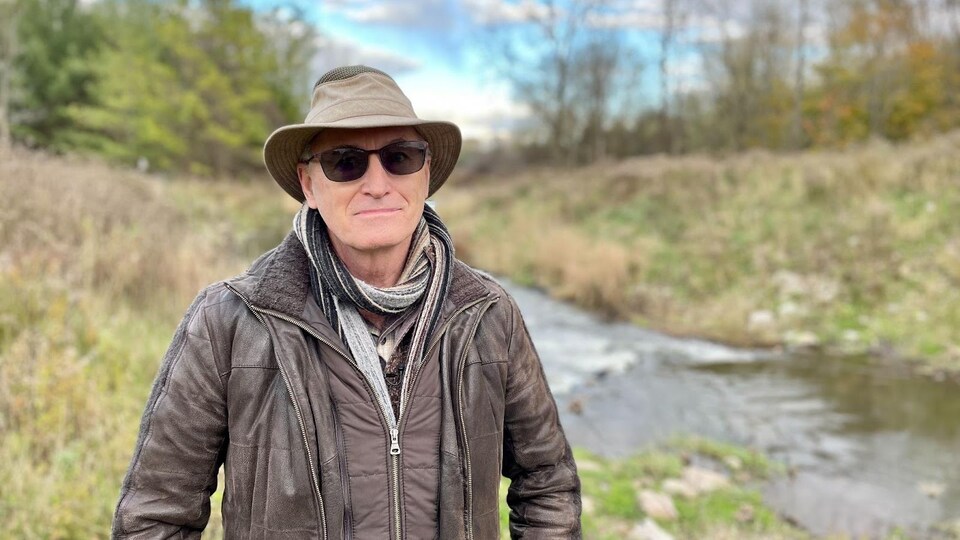 Bryan Smith pose devant un ruisseau, avec un chapeau et des lunettes fumées.