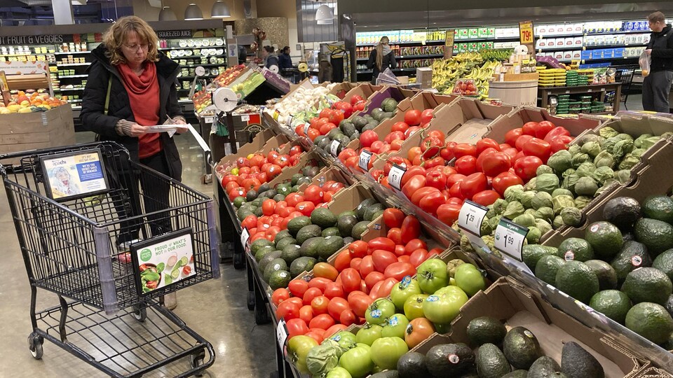 Une cliente consulte sa liste d'épicerie devant un étal de légumes frais.
