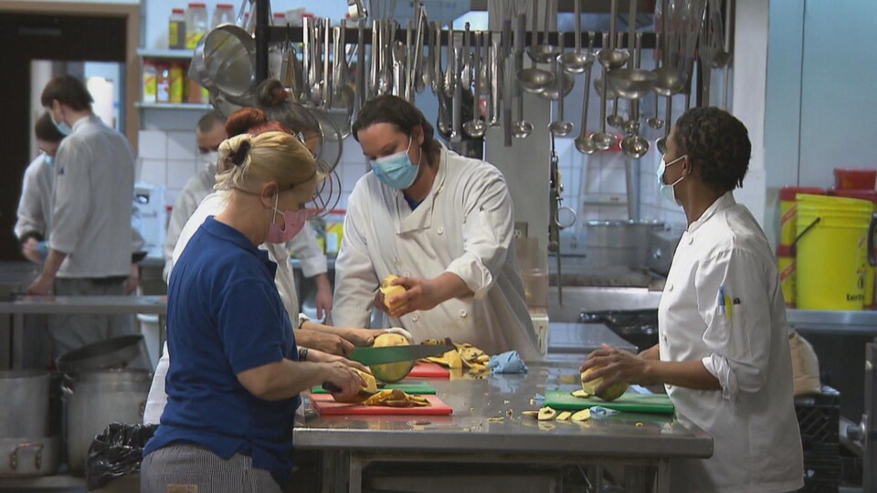 Trois personnes découpent des légumes à une table de travail.