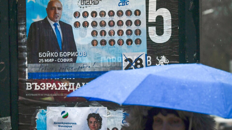 Une femme portant un parapluie passe devant une affiche électorale.