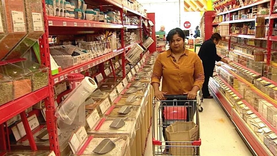 Une femme pousse un chariot dans une allée dans un magasin.