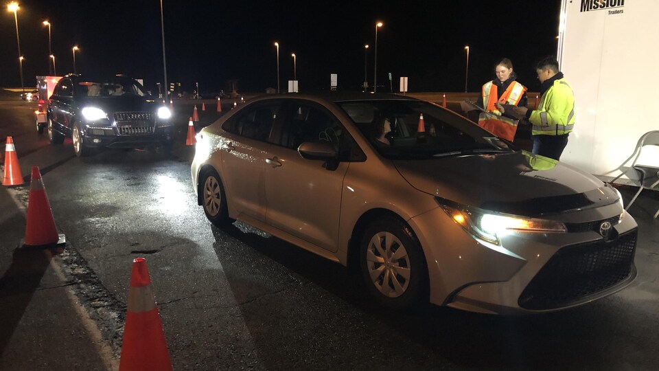 Deux agents provinciaux discutent avec une femme assise au volant de sa voiture.
