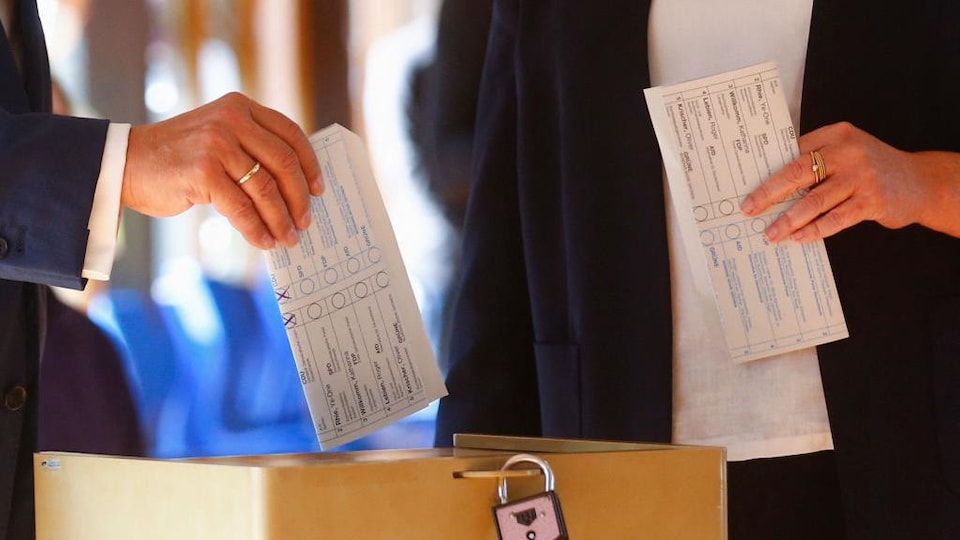 Une main tient un bulletin de vote sur lequel on peut voir deux « X » tracés au crayon.