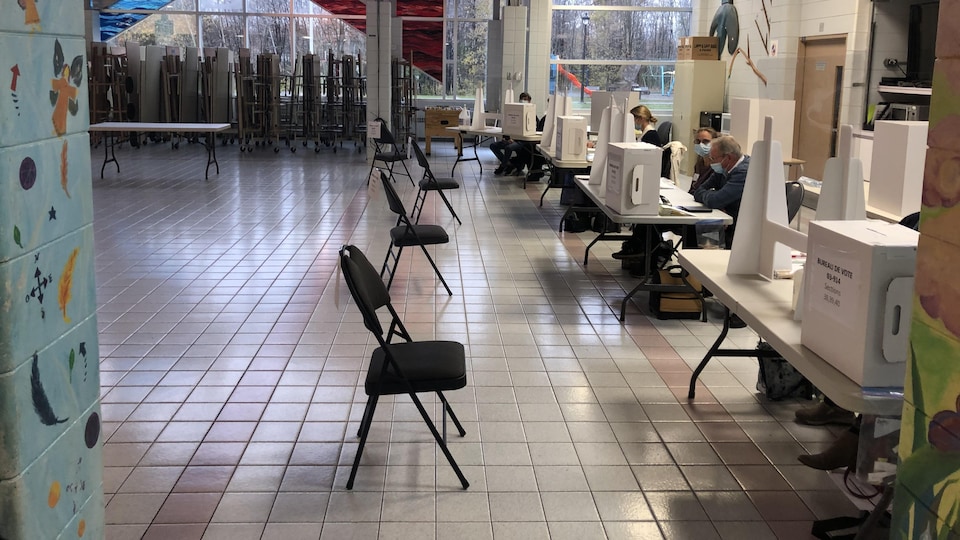 Un bureau de vote désert : des chaises vides sont alignées en face de tables sur lesquelles sont posées des urnes.