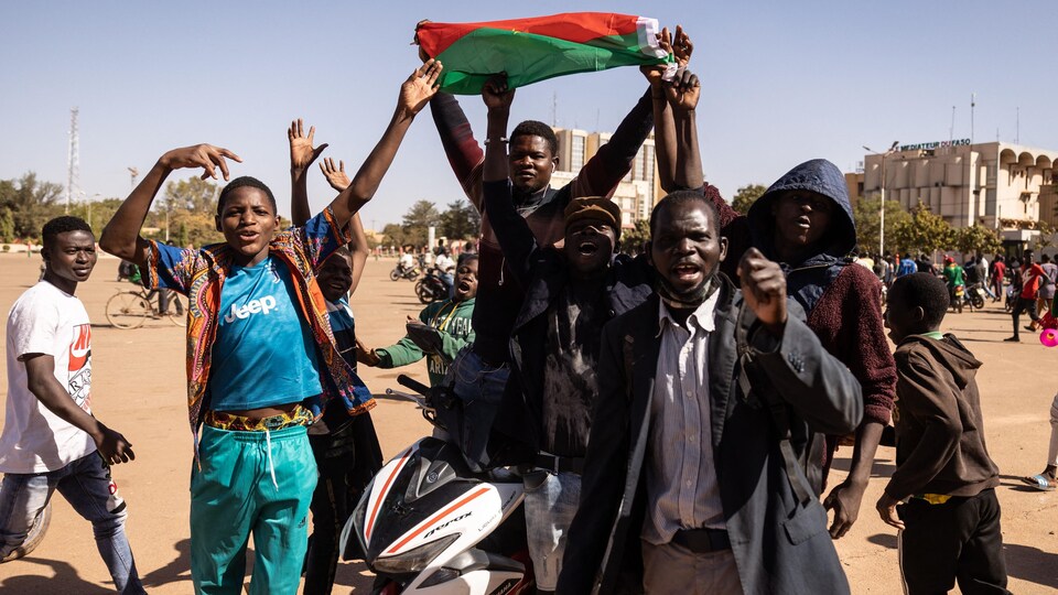 Des gens dans la rue semblent célébrer avec un drapeau du Burkina Faso.