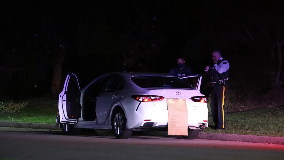 Deux policiers sont debout devant une voiture immobilisée sur la route.
