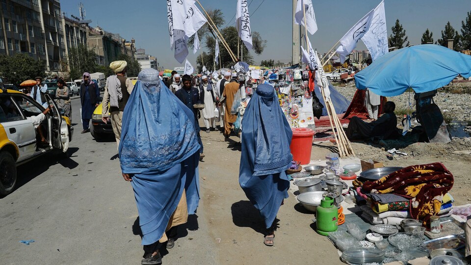 Deux femmes afghanes marchent près d'étals dans un marché, chacune vêtue d'une burqa bleue.